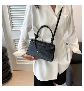 Detail of elegant black crocodile pattern handbag with curved handle and metal accents