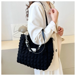 Detail of black quilted shoulder bag with faux pearl chain and floral charm on a model