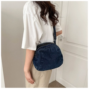 Detail of blue denim crossbody bag showing curved structure and zipper closure on model