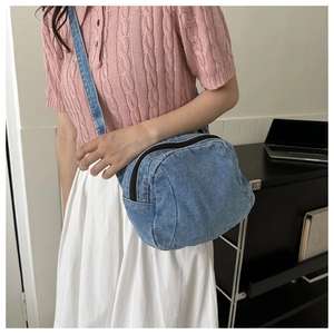 Detail of blue denim crescent crossbody bag shown on model with polished zipper hardware