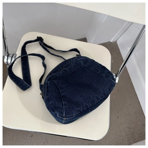 Detail of blue denim crossbody bag with adjustable strap on a cream chair