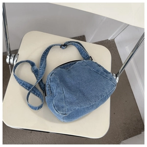 Detailed macro view of light blue denim fabric texture and black zipper on crossbody bag