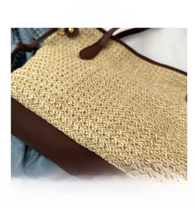 Detail of woven straw tote bag with brown leather trim and handles on denim
