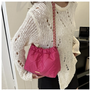 Detail of fuchsia quilted bucket bag with gold chain strap and elegant metal logo plaque