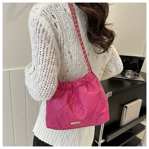 Detail of fuchsia quilted crossbody bag with gold chain strap on a white sweater