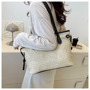 Detail of beige straw tote bag with black leather trim and drawstring on model's shoulder