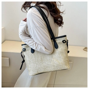 Detail of cream straw tote bag featuring black leather trim and side drawstring tassels