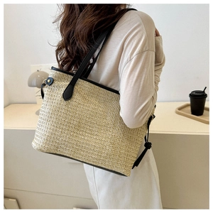 Detailed side view of a large straw tote bag with black leather straps on a model