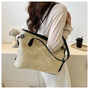 Fashionable straw tote bag with black leather trim worn by model in a minimalist room
