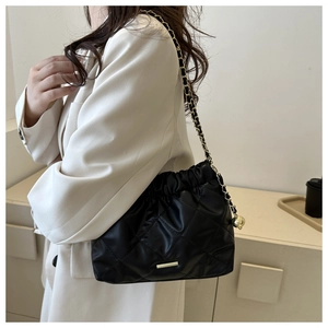 Detail of quilted black shoulder bag with gold chain and decorative metal ball charm