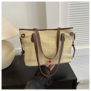 Detail of the woven straw tote bag featuring brown faux leather straps and golden hardware