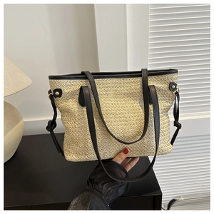 Detail of woven straw tote bag with black faux leather straps and metal rivet accents