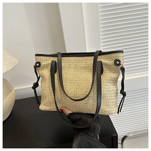 Detail of beige straw tote bag with black leather trim and tassel on shoulder strap
