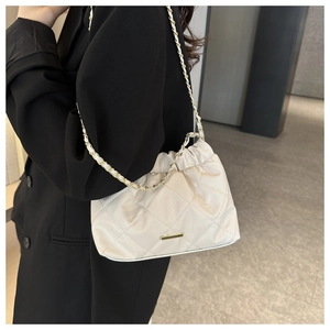 Detail of creamy white quilted tote bag with gold chain strap and metal clasp on black suit