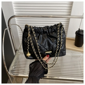 Detail of black quilted shoulder bag featuring gold chain strap and heart charm