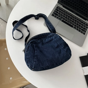 Fashionable dark blue denim half-moon crossbody bag with adjustable strap on desk