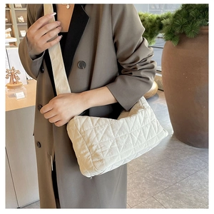 Detail of cream quilted crossbody bag with large diamond stitching on model with blazer