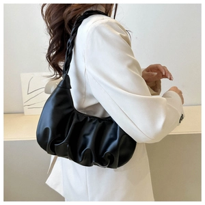 Detail of black pleated shoulder bag featuring a stylish woven strap on a female model