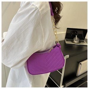 Detail of purple V-quilted faux suede shoulder bag with gold chain strap on model