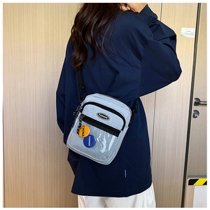 Detalle del bolso bandolera de nailon azul claro con insignias de moda y cremalleras negras
