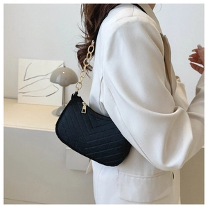 Detail of black V-quilted shoulder bag featuring gold chain strap on model in modern setting