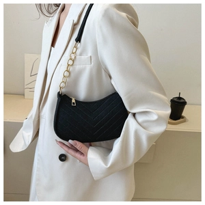 Detail of black quilted hobo bag with gold chain strap on a white blazer outfit