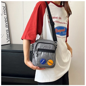 Detalle del bolso bandolera de lona gris con bolsillo de PVC y pines de colores