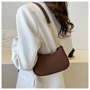 Detail of dark brown suede shoulder bag with gold chain strap on a white blazer