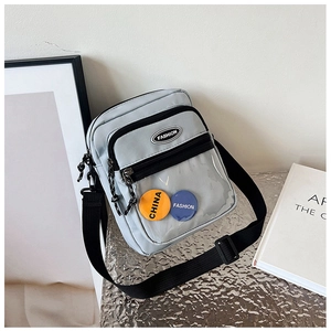 Primer plano del bolso bandolera gris claro con bolsillo de PVC y chapas decorativas