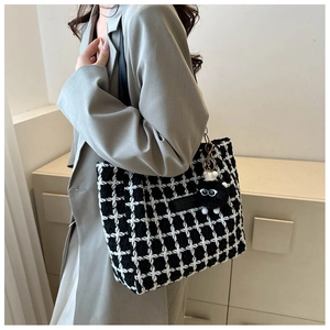 Detail of black and white plaid tote bag with fur charm on a gray blazer model