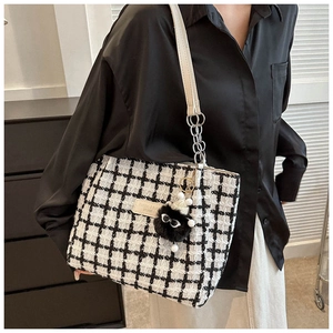 Close-up of checkered tweed tote bag featuring silver chain strap and plush charm