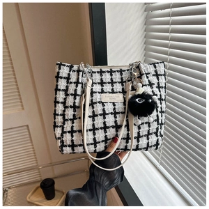 Close-up of black and white tweed tote bag with leather straps and plush charm