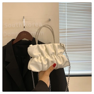 Close-up of white ruched handbag featuring sparkling rhinestone handles and silver chain