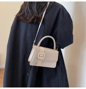 Détail du sac beige avec empiècements pailletés et boucle décorative sur manteau noir