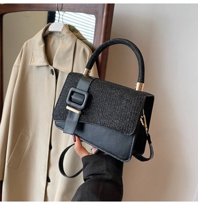 Detailed view of black glitter and leather handbag featuring a large gold square buckle