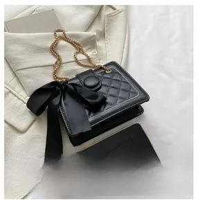 Detail of black quilted leather bag with large satin bow and gold chain strap