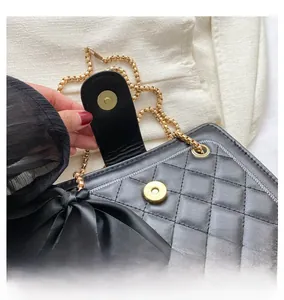Close-up of golden metal magnetic clasp and large black bow on quilted chain bag