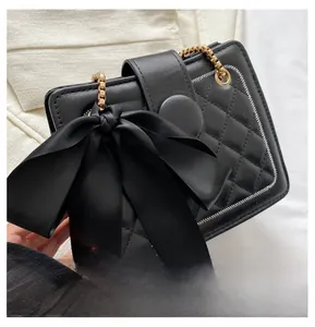 Detail of black quilted shoulder bag featuring a large satin bow and gold chain strap