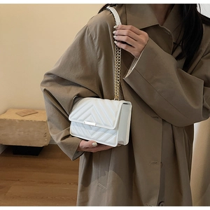 Detail of white V-quilted faux leather shoulder bag with gold chain strap on a brown coat