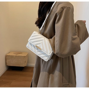 Close-up of white V-quilted small square bag with golden chain strap and metal buckle