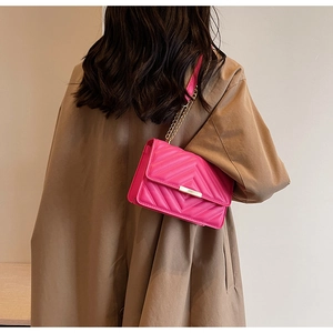 Close-up of rose red crossbody bag with V-shaped quilting and gold metal chain strap