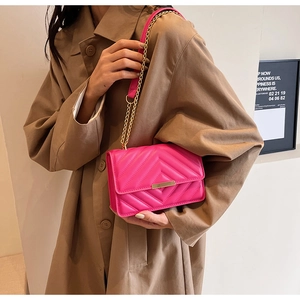 Detail of hot pink quilted chain bag with gold metal clasp on a beige trench coat