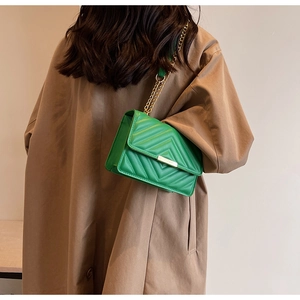 Model wearing a vibrant green quilted chain shoulder bag against a khaki trench coat
