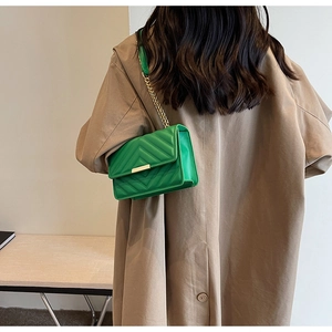 Side view of vibrant green quilted crossbody bag with gold chain strap on model