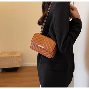 Detail of caramel quilted shoulder bag with gold chain strap worn with a black blazer
