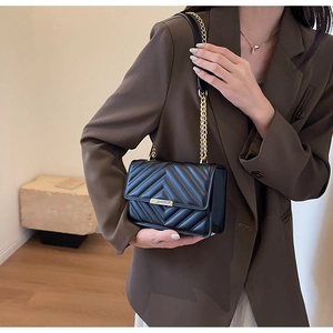 Detail of black quilted crossbody bag with gold chain strap and metallic buckle