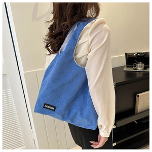 Détail du sac cabas en velours côtelé bleu avec étiquette porté à l'épaule du mannequin