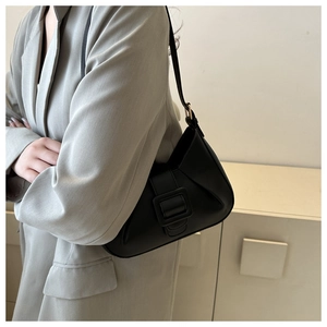 Side view of a black matte crescent bag with a large square buckle worn on the shoulder