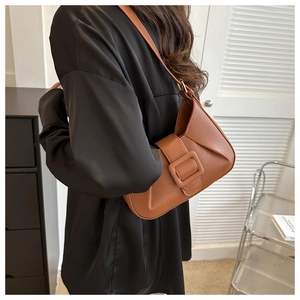 Detail of caramel brown faux leather underarm bag featuring a large square buckle and pleats