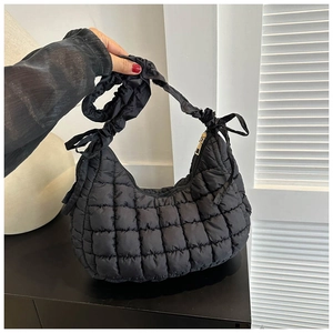 Detail of black quilted shoulder bag with knotted strap and gold-tone zipper closure